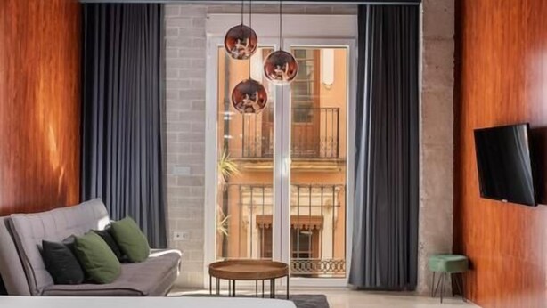 Una habitación de hotel moderna con una cama grande, una mesita pequeña y un televisor montado en la pared.
