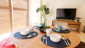 A dining table set with bowls, spoons, forks, and wine glasses, with a TV and plant in the background. - Mainichi Building Osaka (Osaka)