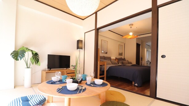 A modern room with a dining table set for two, a TV, and a bed with a blue bedspread. - Mainichi Building Osaka (Osaka)