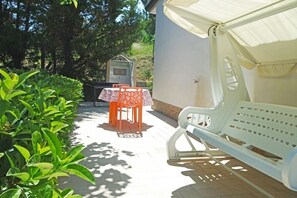 A patio with a white bench, a table with a patterned tablecloth, and a grill in the background. - Casa Elena (Ascea)