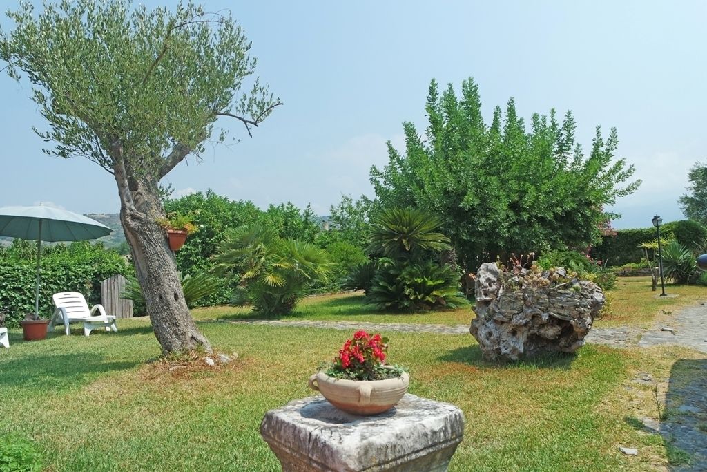 Ein Garten mit Steinpflanzgefäß, Baum und weißem Stuhl.
