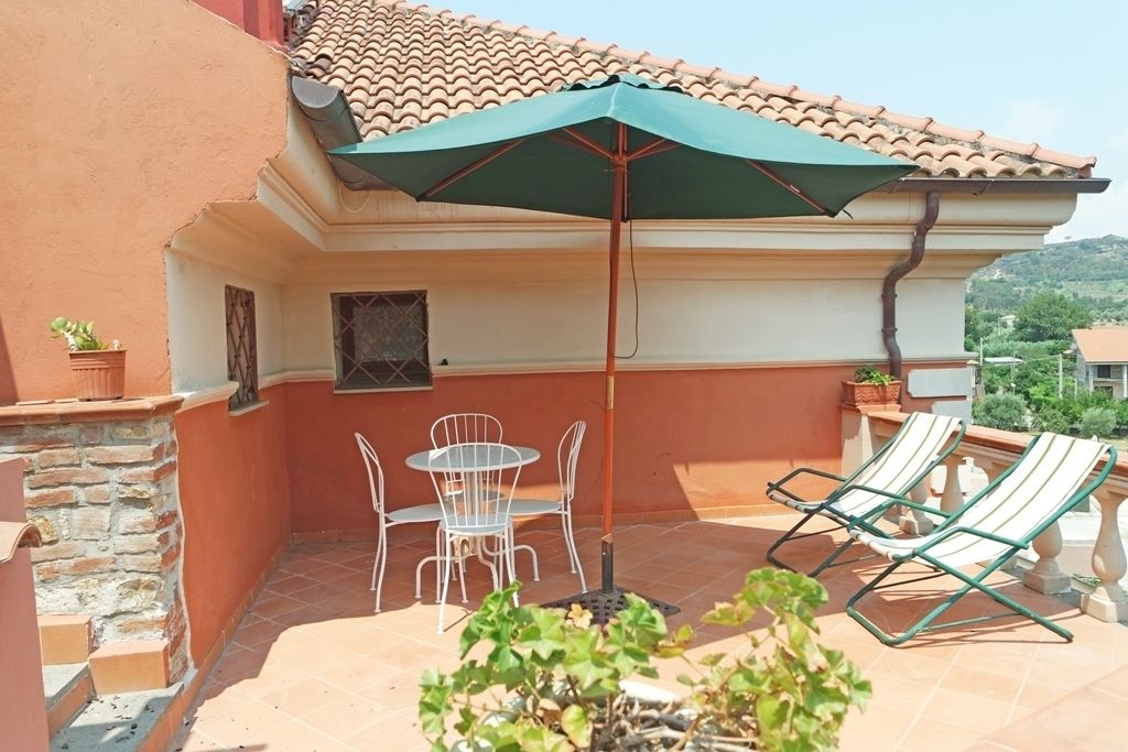 An outdoor patio with a table and chairs, a green umbrella, and two lounge chairs.