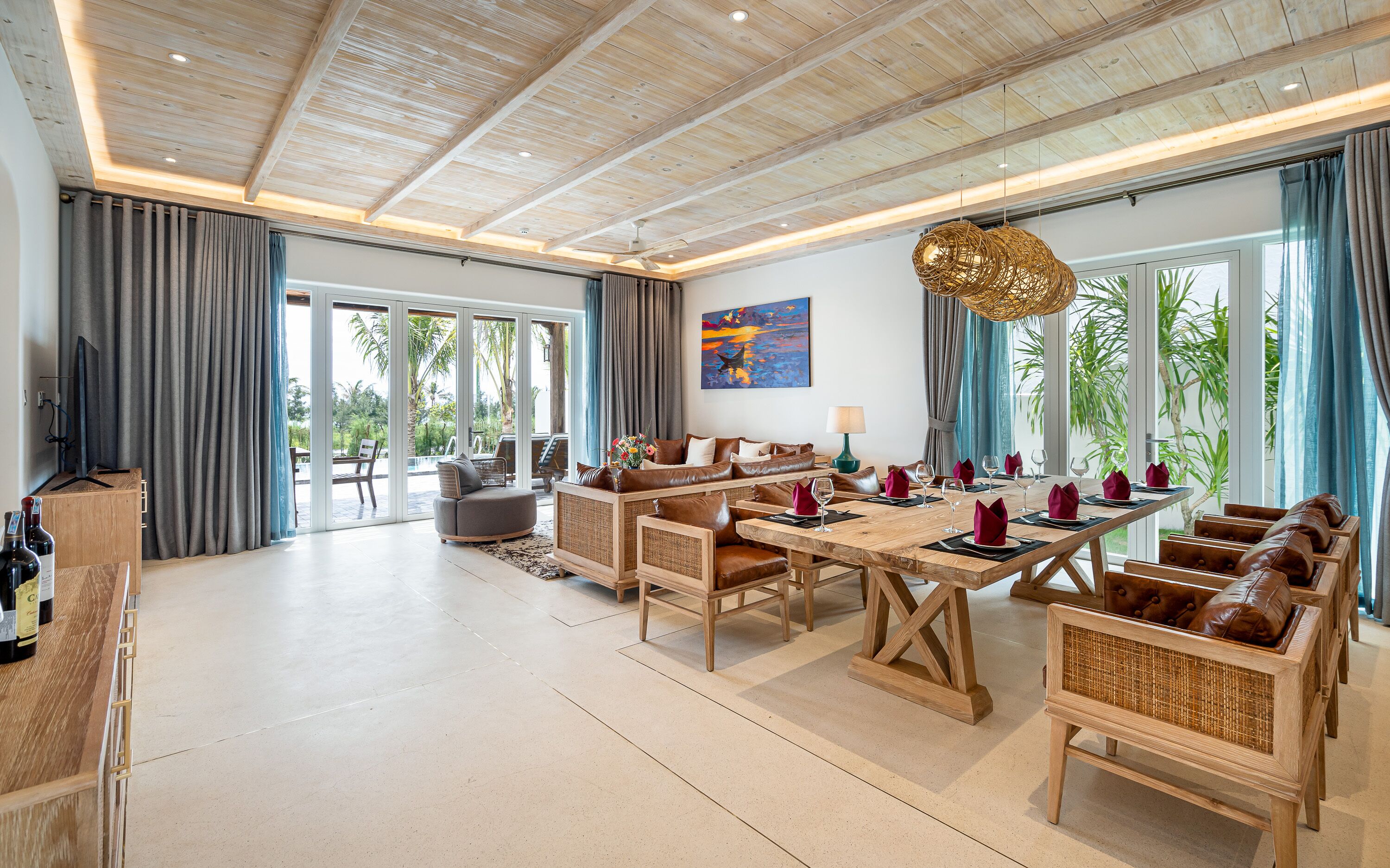 A spacious living area with a wooden ceiling, a dining table set for six, and a large window with curtains.