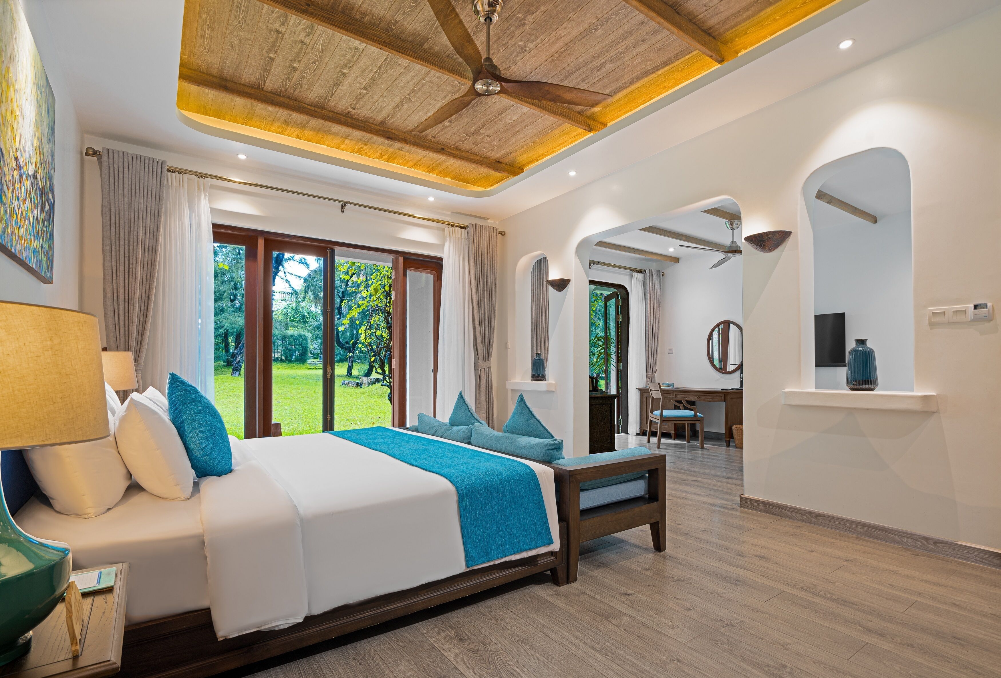 A spacious bedroom with a large bed, a wooden ceiling fan, and a view of the garden through the sliding doors.