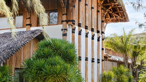 Un bâtiment moderne doté d’un toit de chaume, de lambris en bois verticaux et d’une végétation luxuriante.