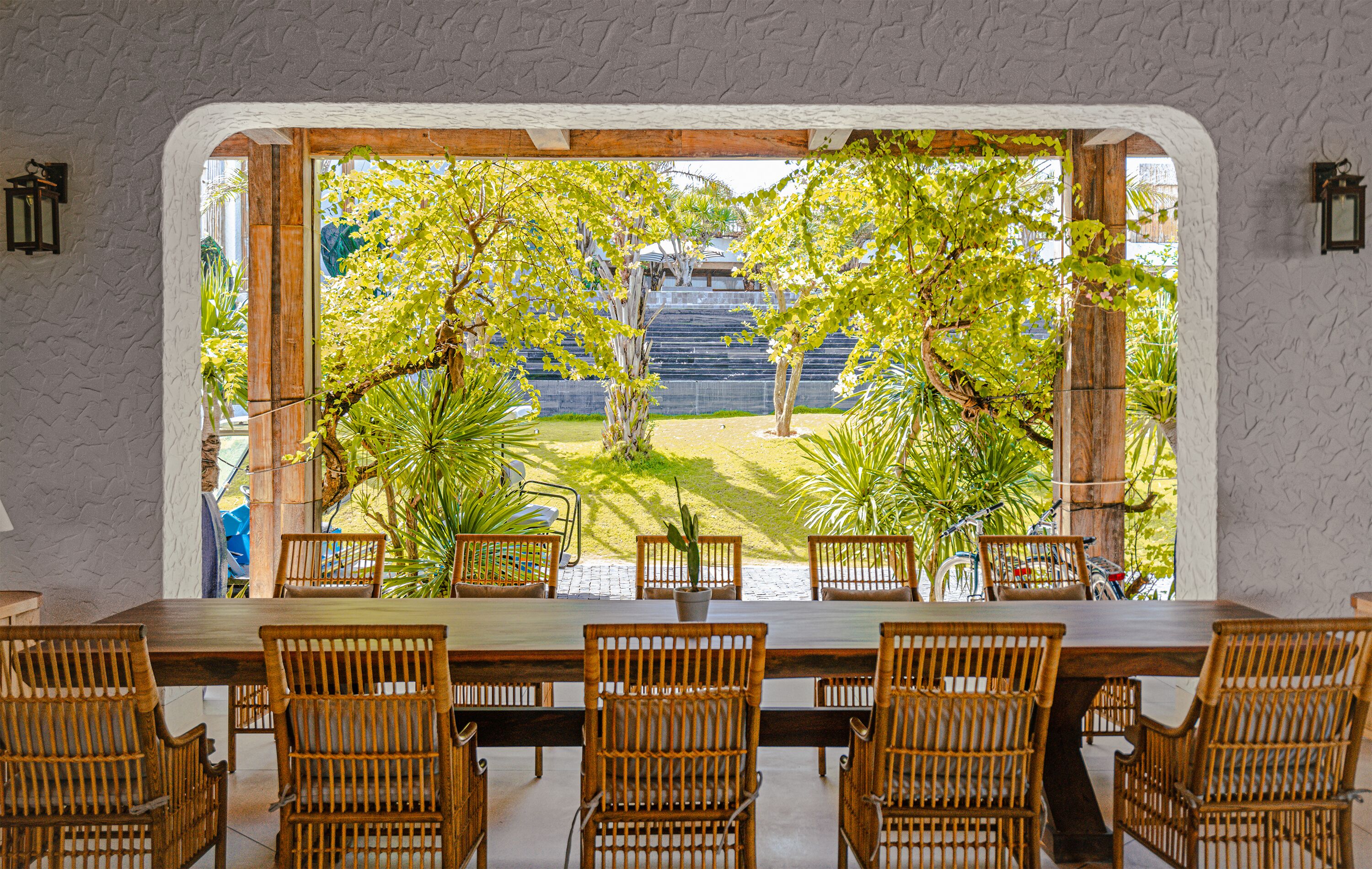 Zona pranzo con vista su un giardino attraverso un'ampia finestra ad arco.