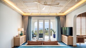 Une chambre d’hôtel avec un grand lit, un ventilateur de plafond, une télévision et un balcon offrant une vue sur l’océan.