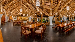 Un vaste espace intérieur doté de hauts plafonds et de poutres en bois, aménagé avec différents types de sièges, notamment des tables et des bancs.
