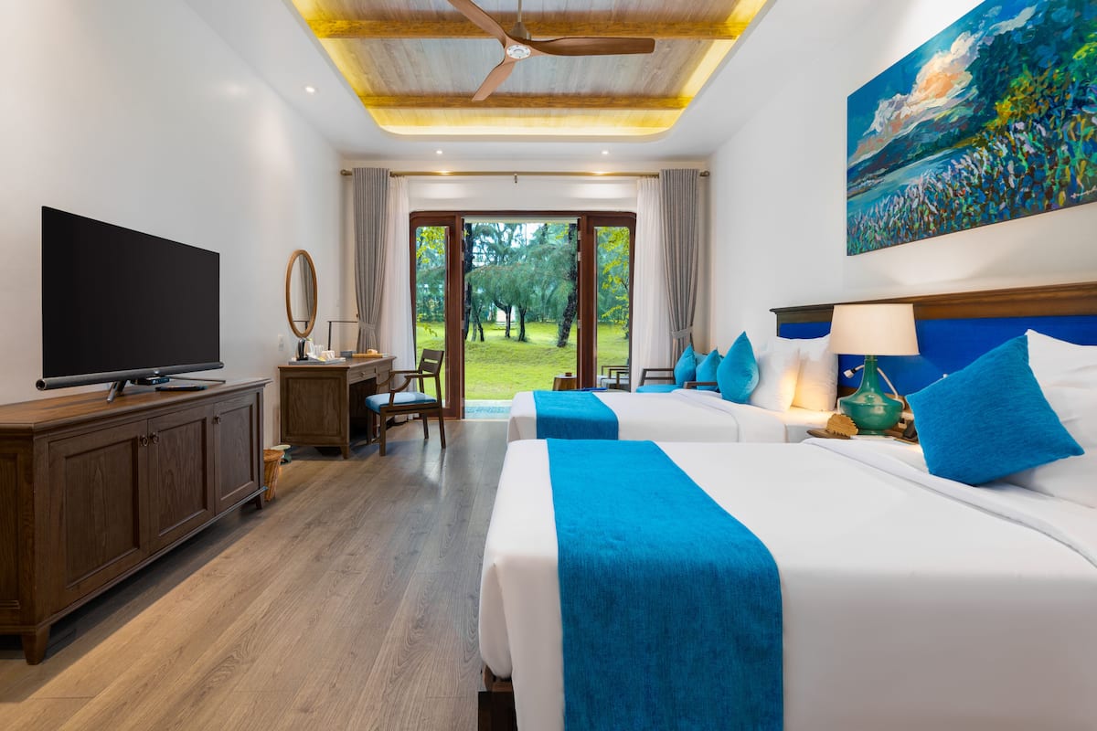 A hotel room with two beds, a TV, a desk, and a painting.