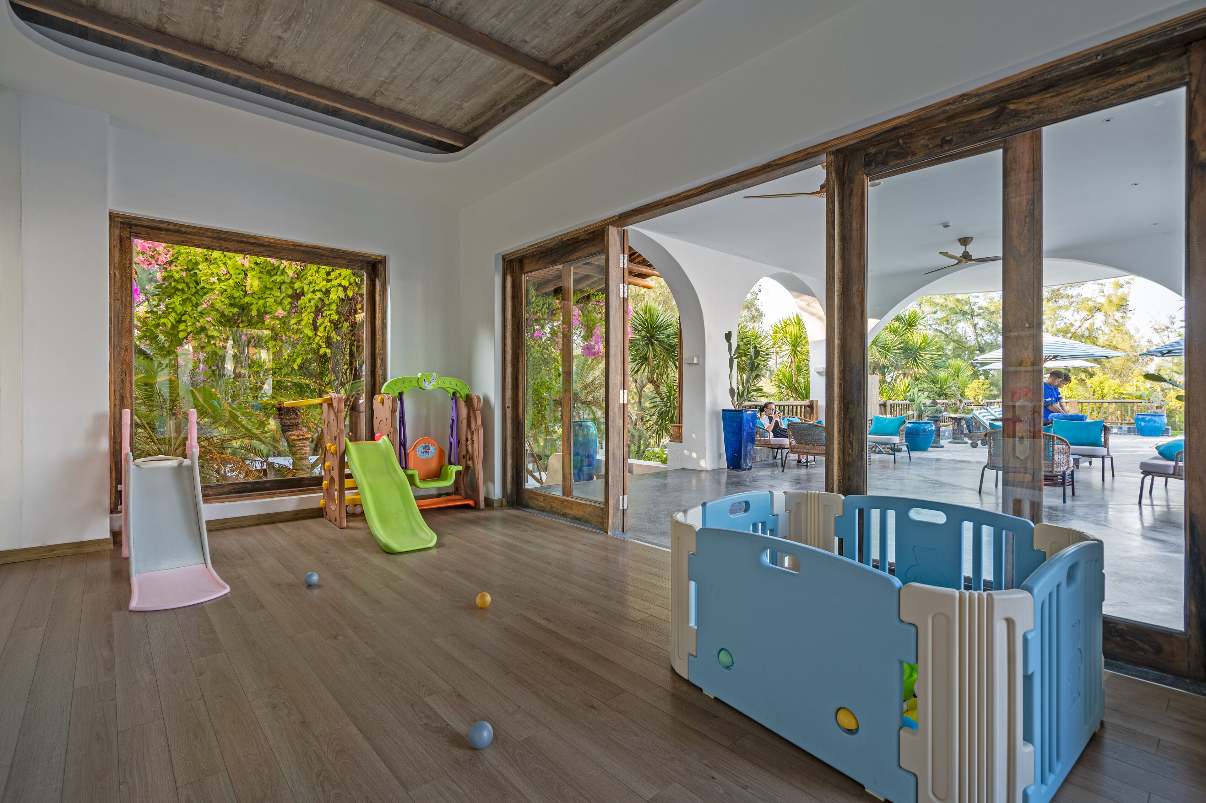 A spacious indoor play area with a slide, playpen, and open patio with outdoor seating.