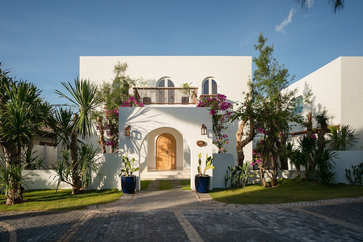 A building with a white facade, a wooden door, and a balcony with plants.