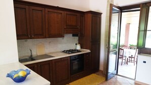 A kitchen with wooden cabinets, a gas stove, a sink, and a yellow rug. - Villa Kalithea (Montecorice)