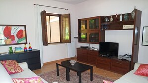 A living room with a sofa, a coffee table, a TV, a cabinet with glass doors, and a window with curtains. - Villa Kalithea (Montecorice)