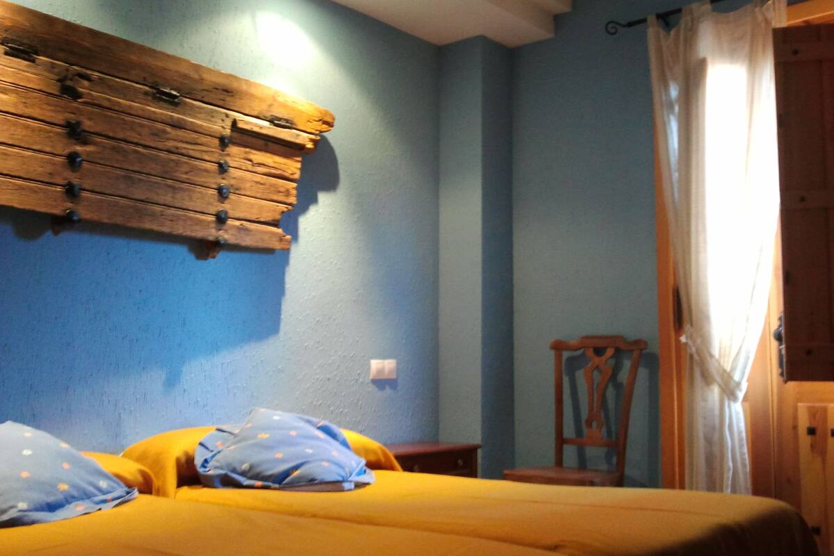 A room with a bed, a wooden headboard, a chair, and a window with curtains.