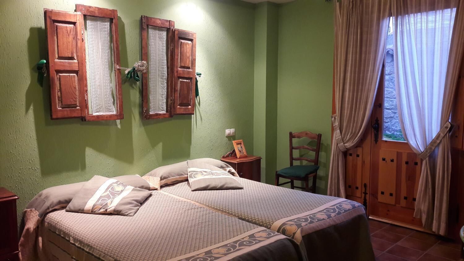Una habitación con dos camas, una puerta de madera, una silla y una ventana con cortinas.