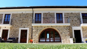A two-story building with stone walls, a balcony, and a large arched entrance. - Casale Acquaviva (Torchiara)