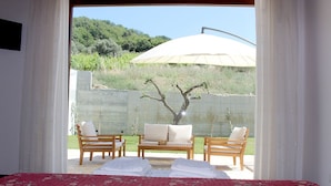 A bedroom with a bed, a red floral bedspread, two wooden chairs, a small table, and an umbrella outside. - Casale Acquaviva (Torchiara)