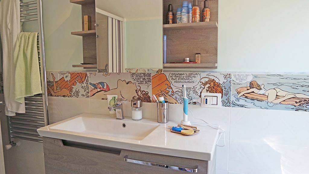 A bathroom with a white sink, a mirror, and a tiled backsplash with cartoon characters.
