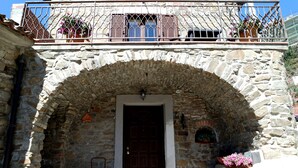 Un edificio de piedra con una puerta de madera, un balcón con barandillas de metal y macetas con flores.