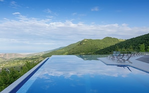 A infinity pool with a clear view of a mountainous landscape and a distant horizon.