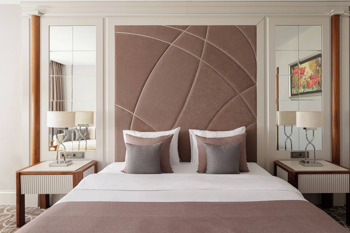 A hotel room with a large bed, two bedside tables with lamps, a large mirror, and a decorative wall panel.