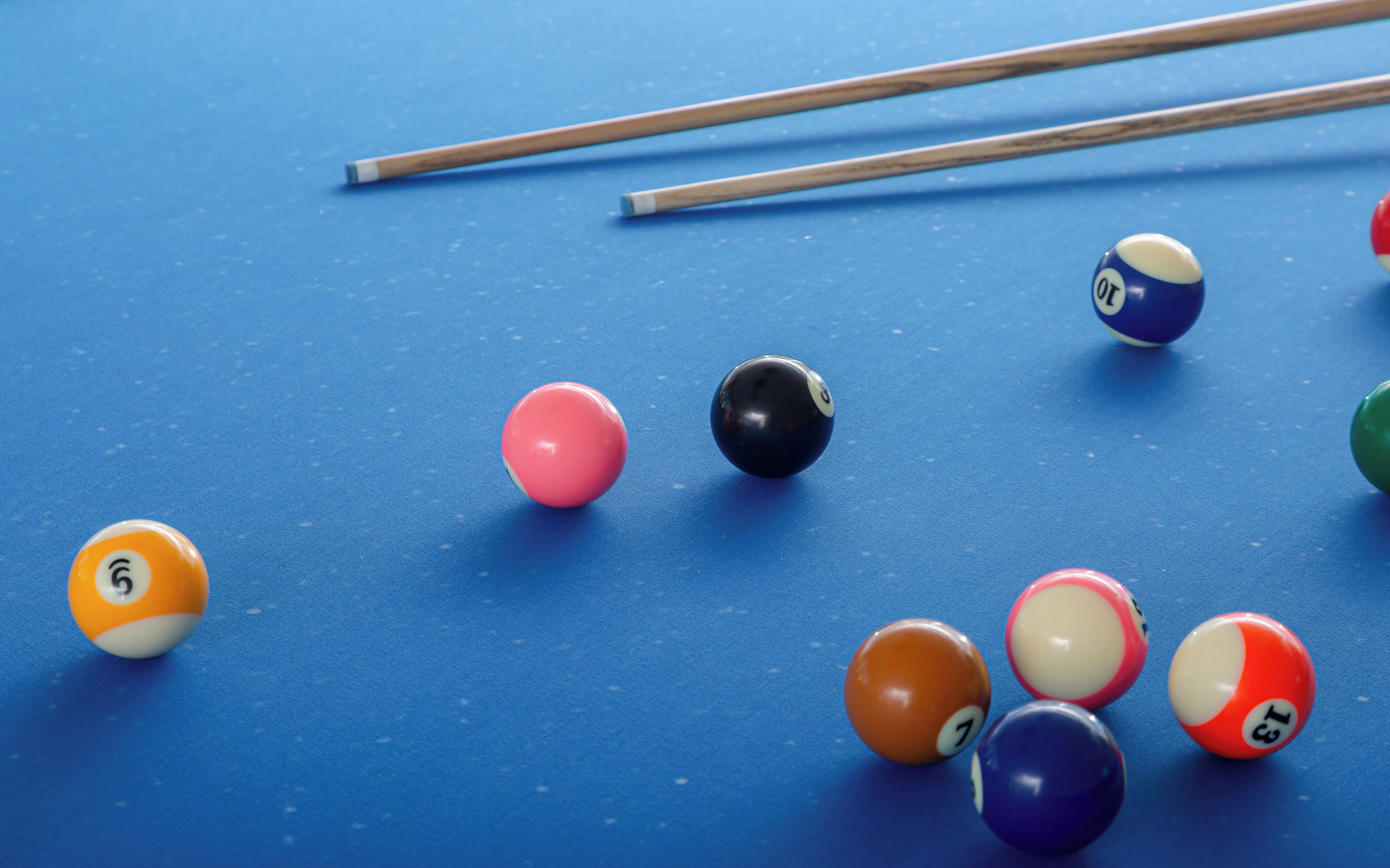 A blue pool table with various colored billiard balls and two pool cues.