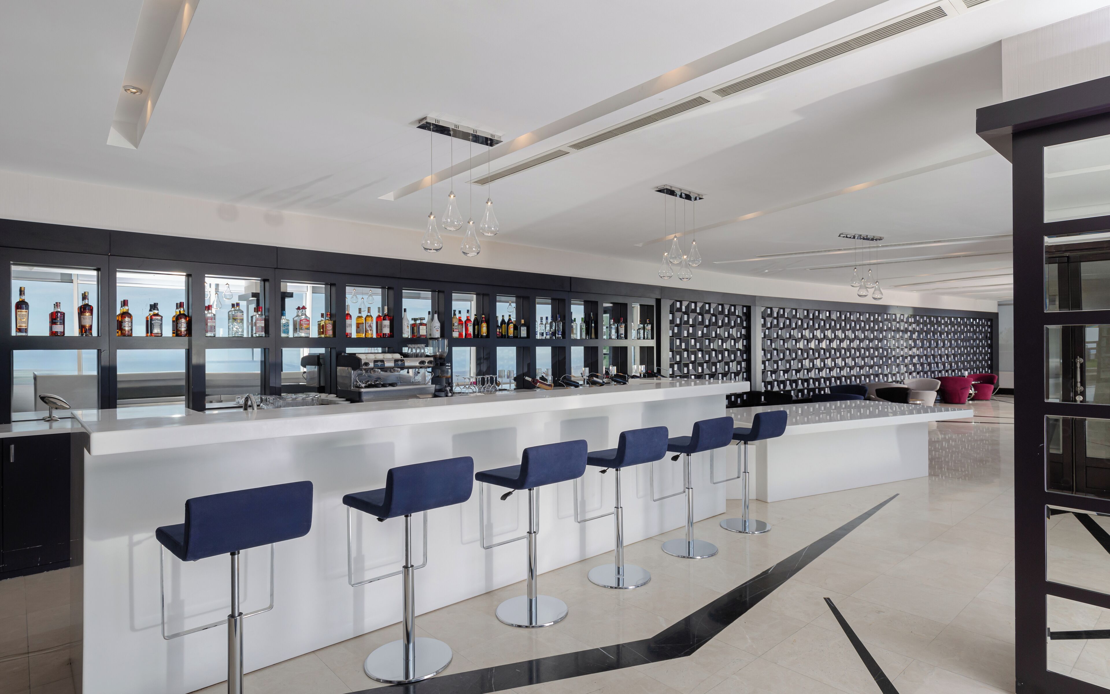 A modern bar area with a long counter, multiple stools, and a variety of bottles and glasses.