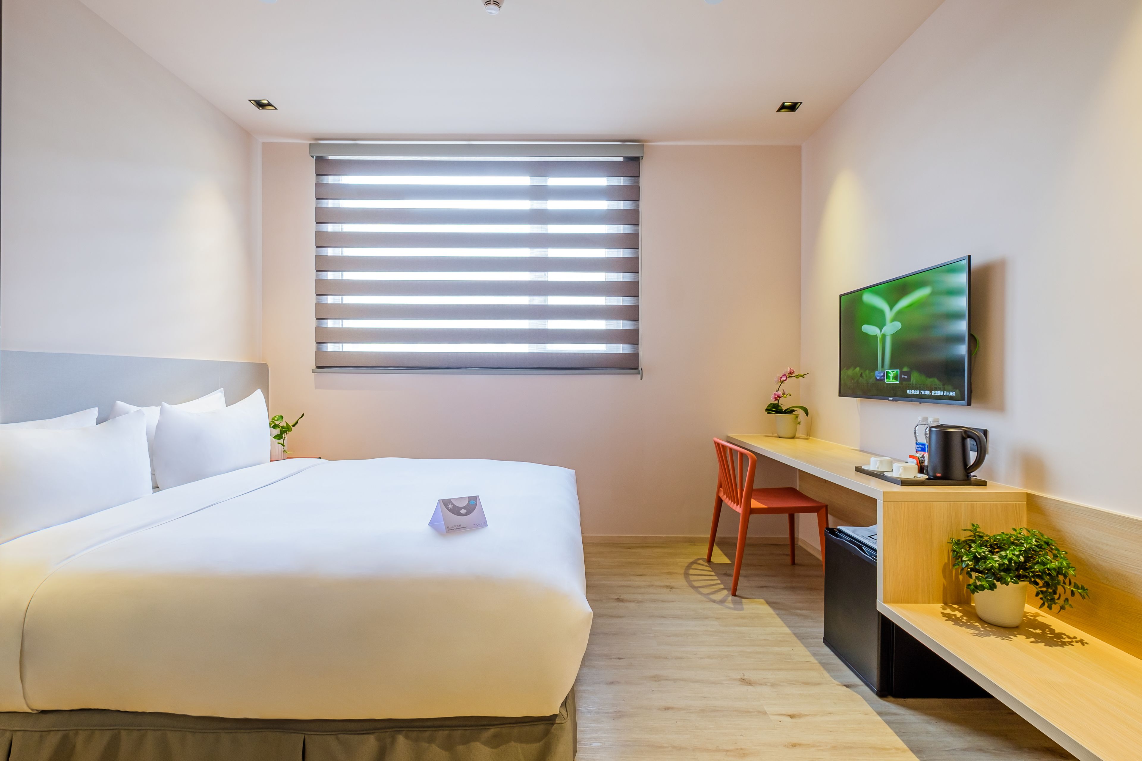 Una camera d'albergo con un letto, una scrivania, una sedia, una televisione e una finestra con tende.