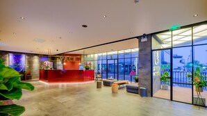 Eine moderne Hotelhalle mit einer Rezeption, einer Sitzecke und großen Fenstern mit Blick auf die Stadt.