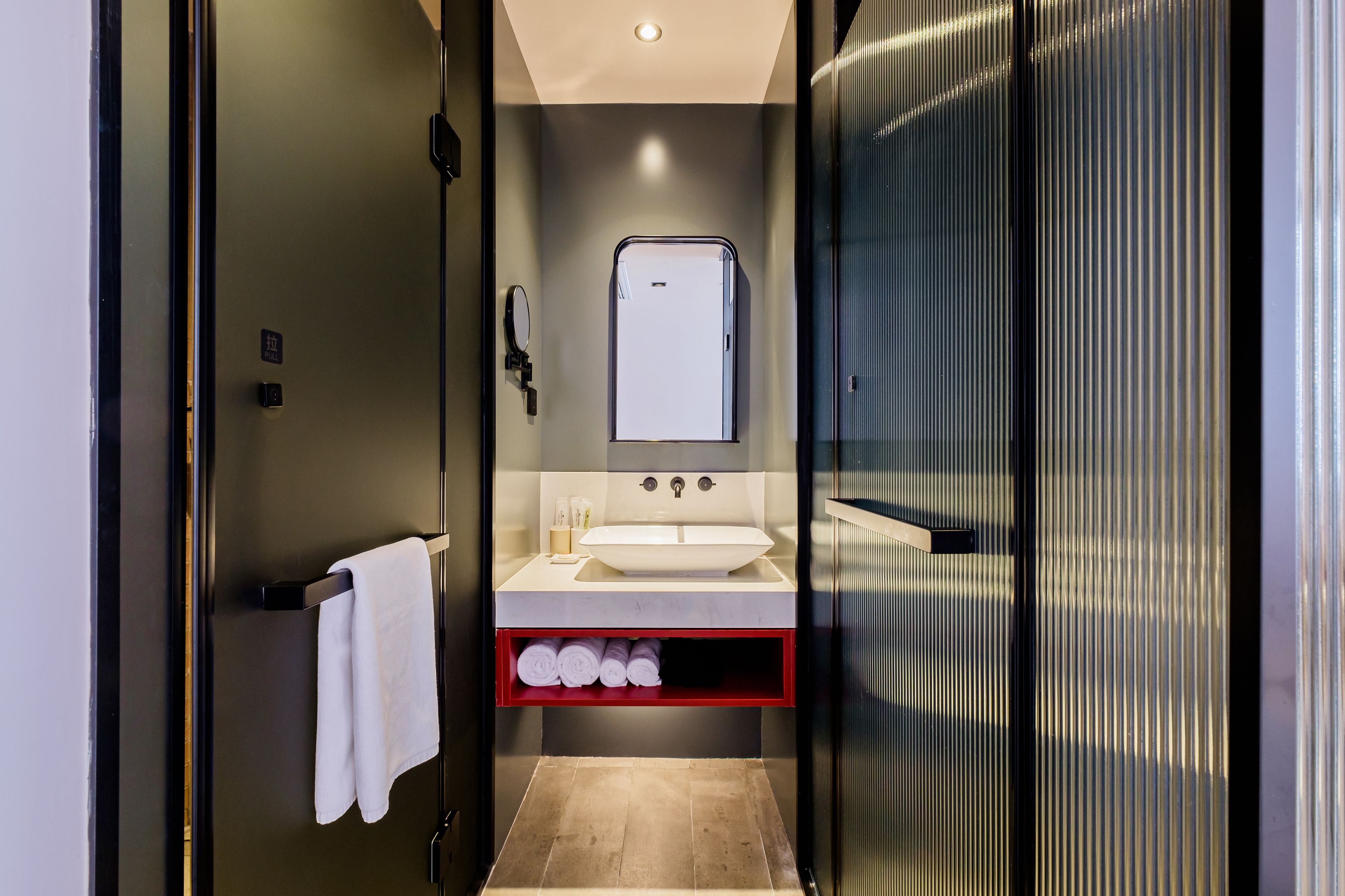 Un baño moderno con un lavamanos blanco, un espejo y un perchero rojo.