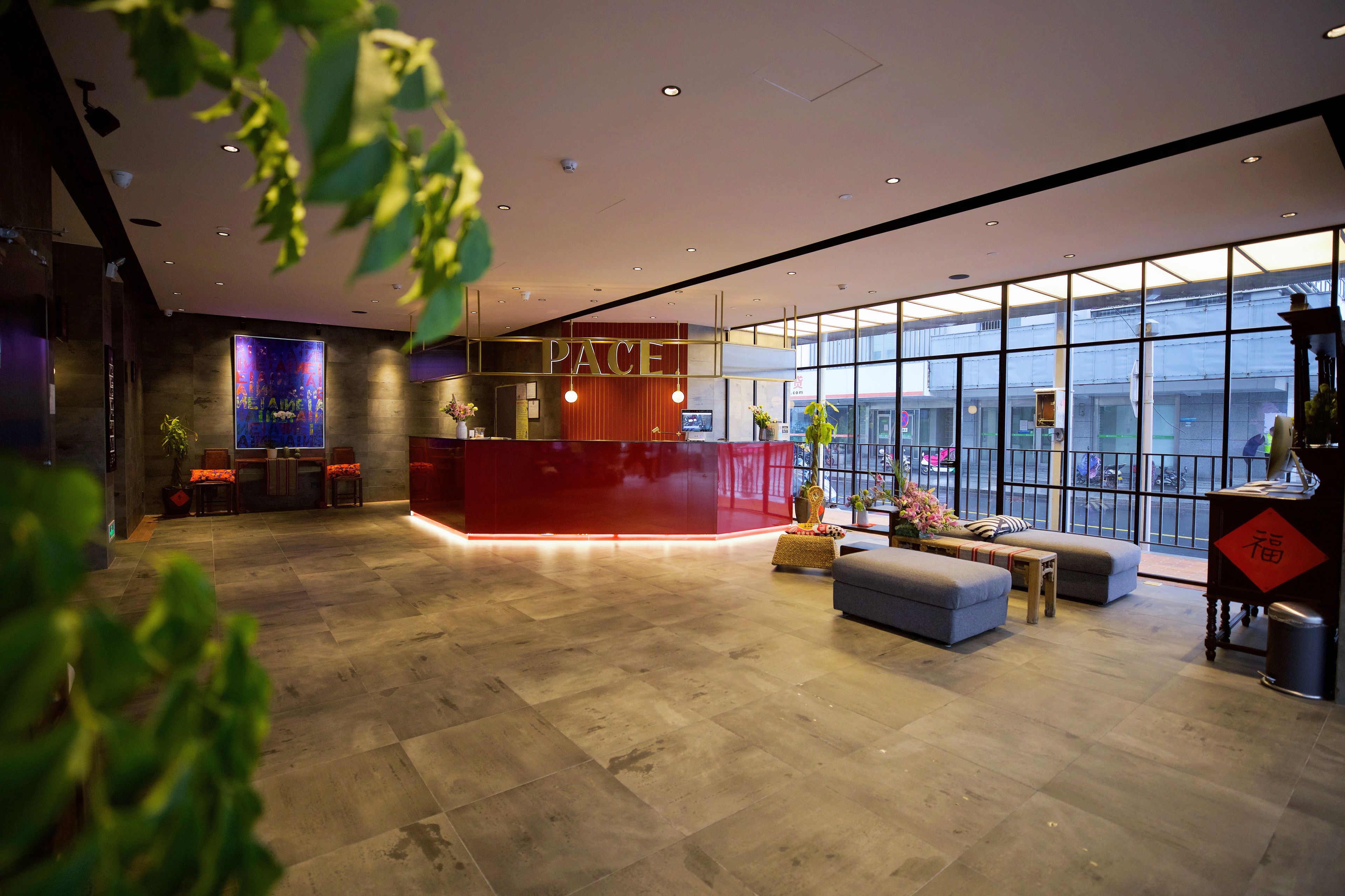 A modern lobby with a reception desk, seating area, and large windows offering a view of the city.