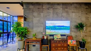 Ein modernes Wohnzimmer mit großem Flachbildfernseher an einer strukturierten Wand, Holzmöbeln und Topfpflanzen.