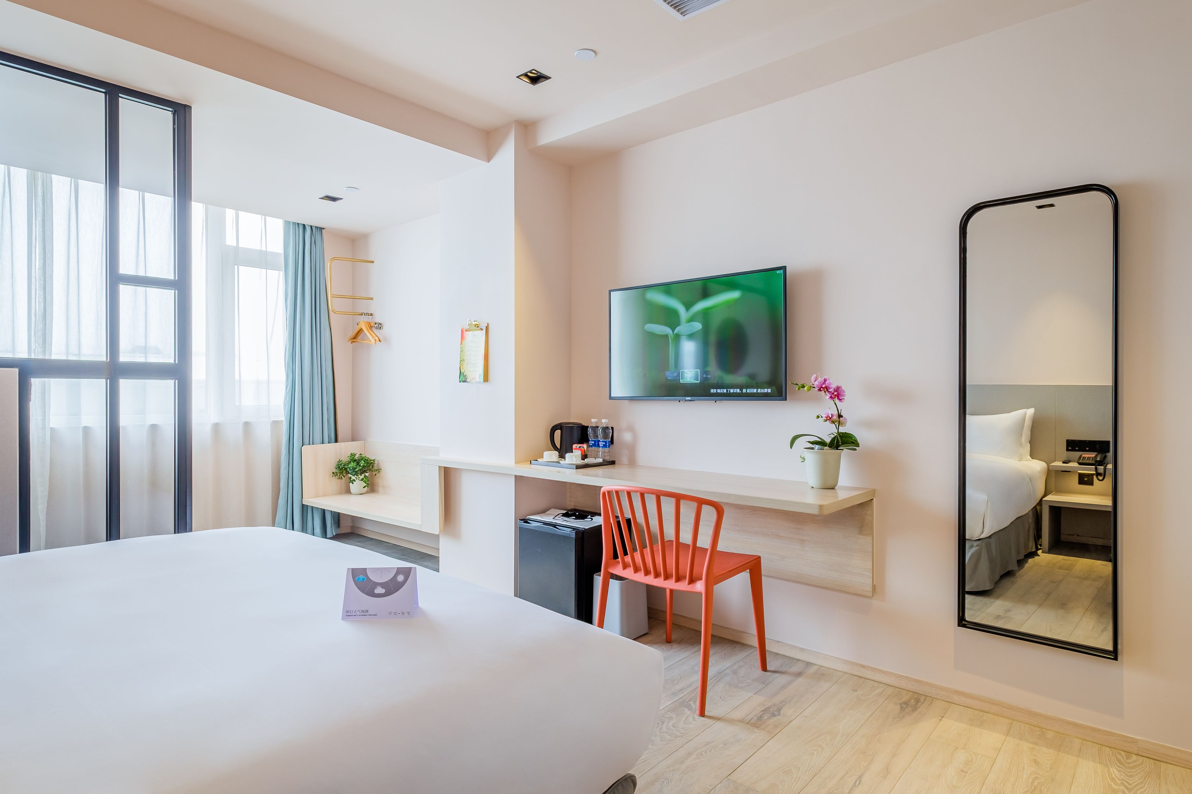 A hotel room with a large bed, a desk with a TV, a chair, and a mirror.