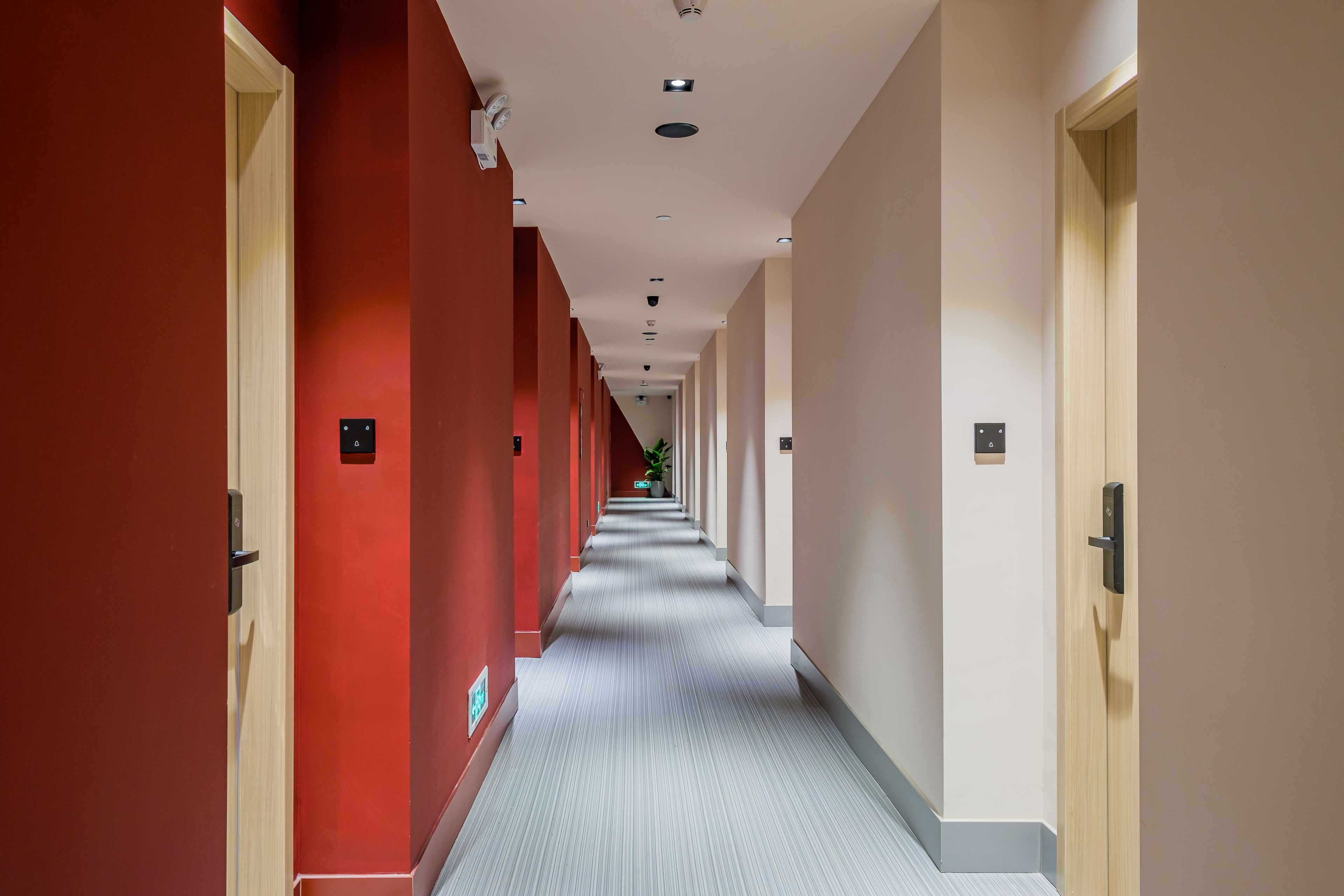 A long, narrow hallway with red and beige walls, a patterned carpet, and doors on both sides.