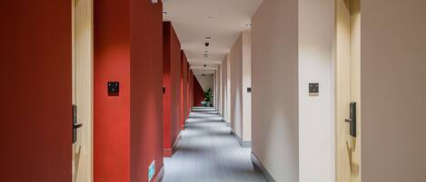 A long, narrow hallway with red and beige walls, a patterned carpet, and doors on both sides.