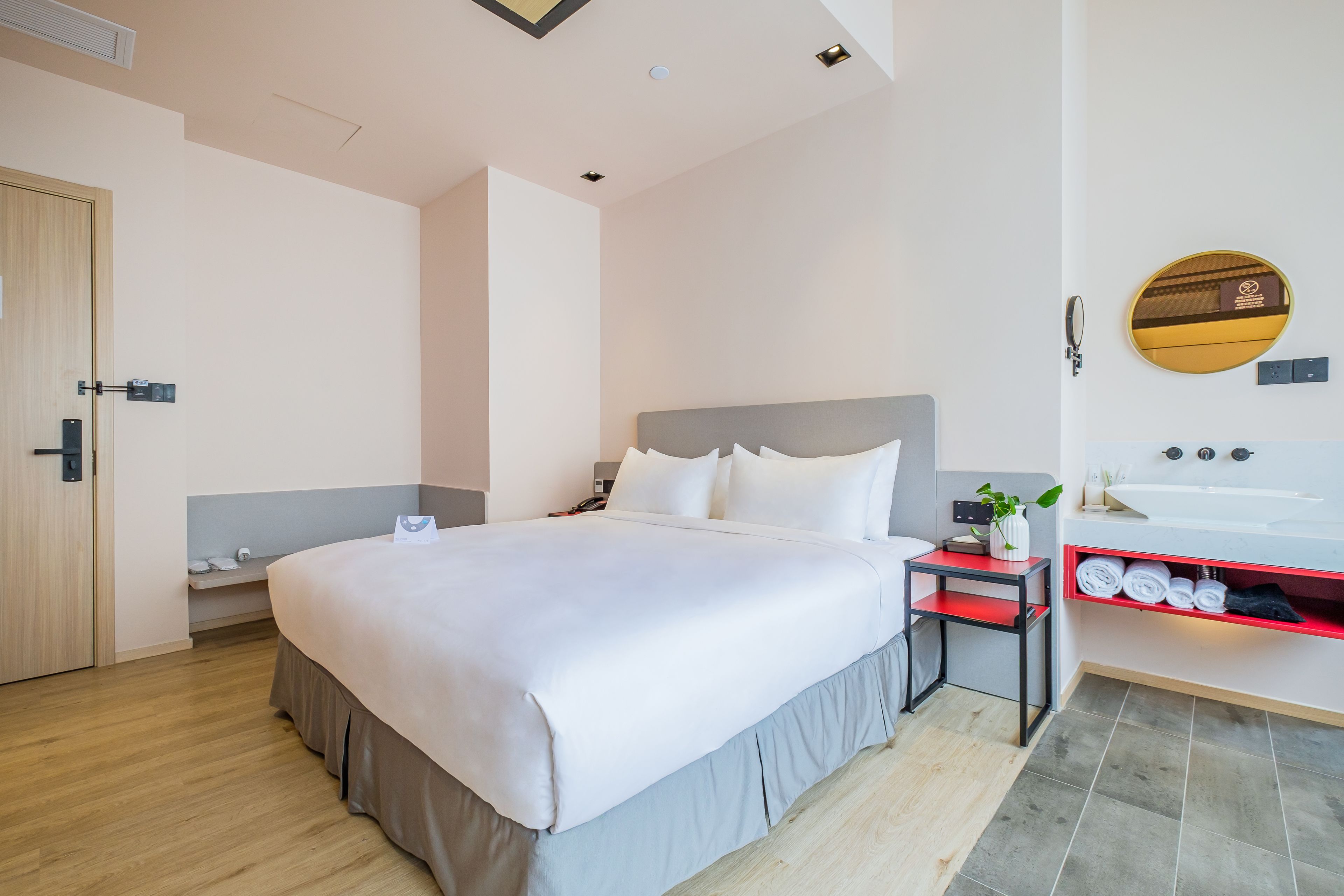 Une chambre d’hôtel moderne avec un grand lit, une table de chevet et une salle de bain équipée d’un lavabo et d’un miroir.