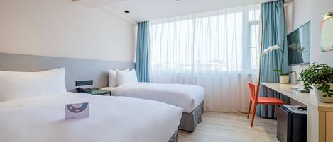 Ein Hotelzimmer mit zwei Betten, einem Schreibtisch, einem Sessel, einem Fernseher und einem Fenster mit Vorhängen.