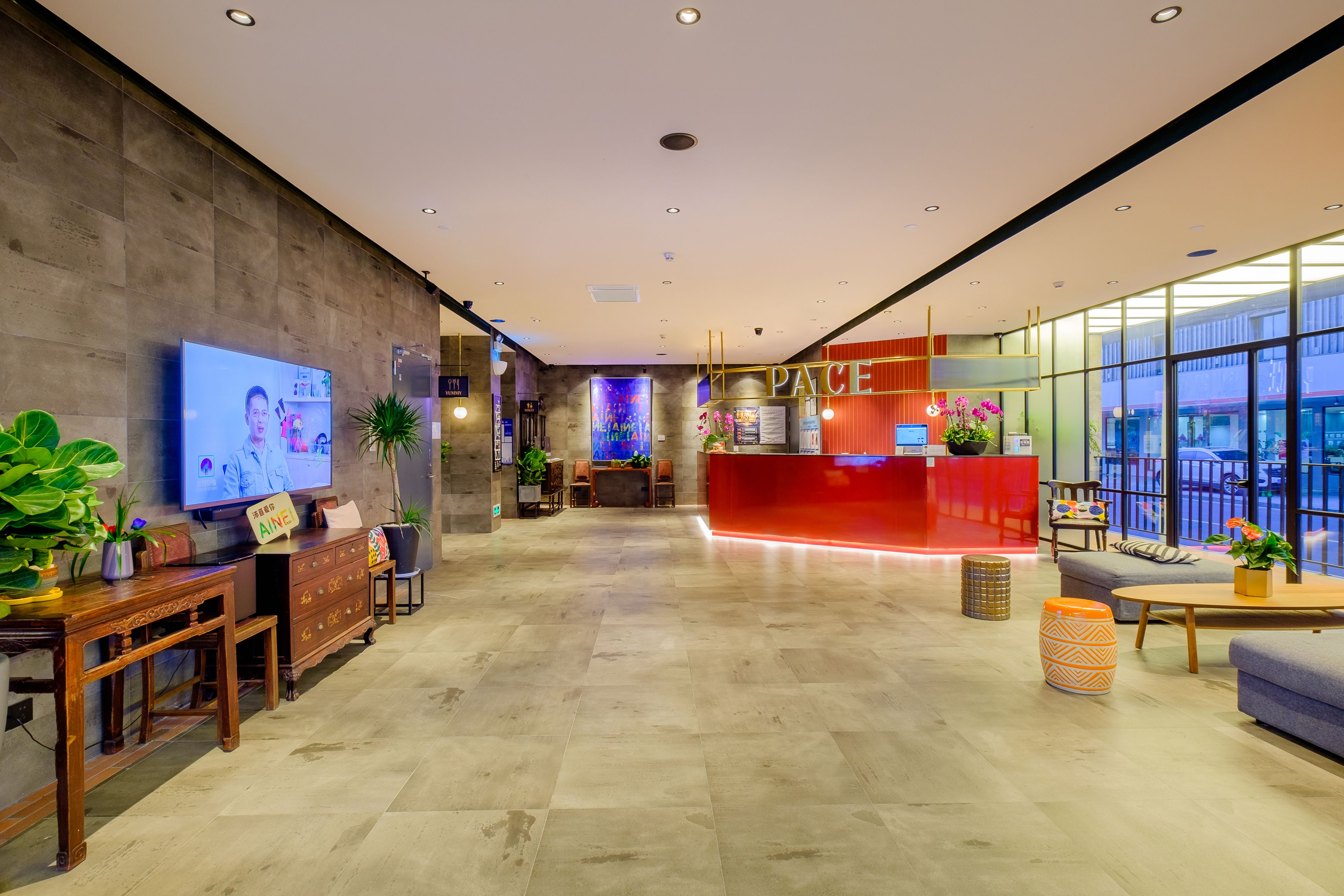 A modern hotel lobby with a reception desk, seating area, and a large TV screen.