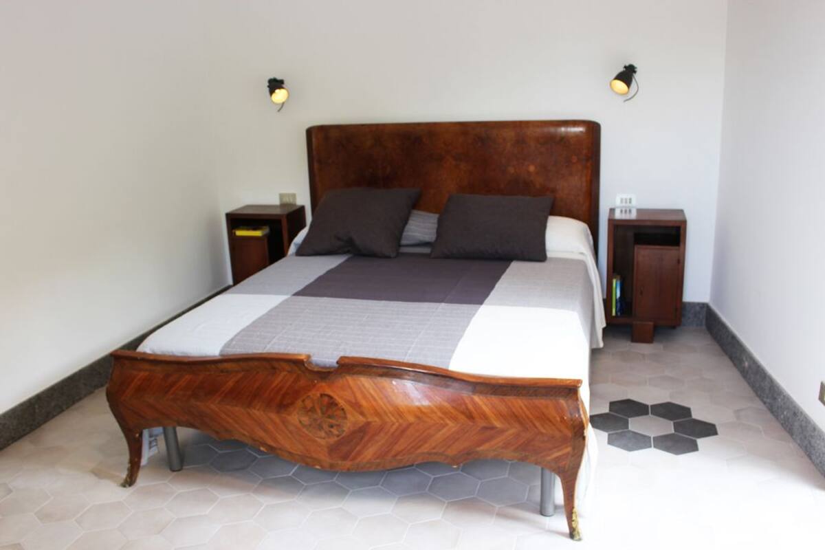 A neatly made bed with a wooden headboard, two bedside tables, and a hexagonal patterned floor.