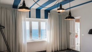 A room with a bed, a desk, and a view of the sea through large windows. - La Concha Suites (Pollica)