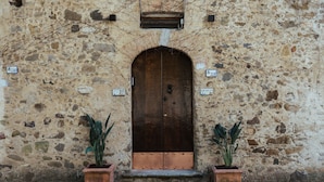 A stone building with a large wooden door, potted plants, and numbered signs. - La Concha Suites (Pollica)
