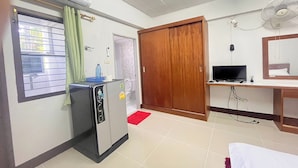 Habitación de hotel compacta con kitchenette, televisión, armario de madera y ventana con cortinas.