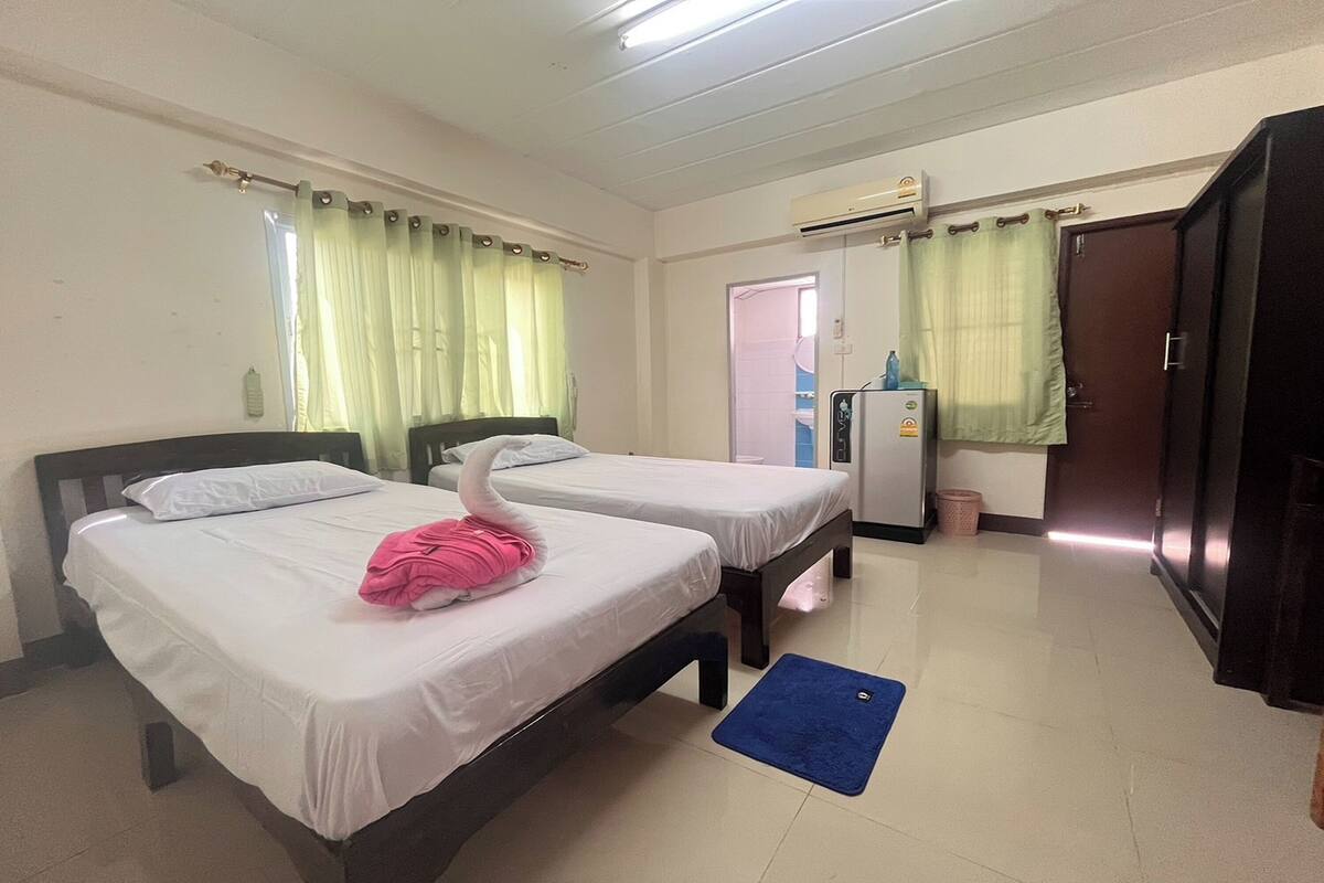Une chambre d’hôtel avec deux lits simples, un tapis bleu, une armoire, un réfrigérateur et une porte donnant sur une salle de bain.