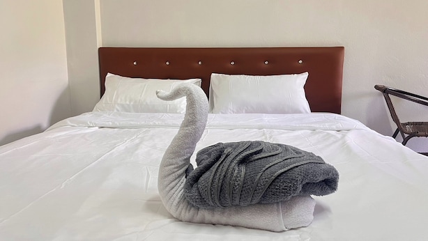 Una cama con cabecera marrón, ropa de cama blanca y una toalla con forma de cisne sobre la cama.