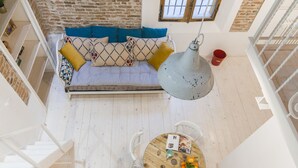 A high-ceilinged room with a wooden floor, a white sofa with patterned cushions, a round wooden table with chairs, and a hanging light fixture. - University Loft Apartment (Bologna)
