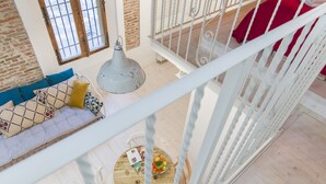 A high-ceiling room with a wooden floor, a white railing, a red bed, and a round wooden table with a bowl of fruit. - University Loft Apartment (Bologna)