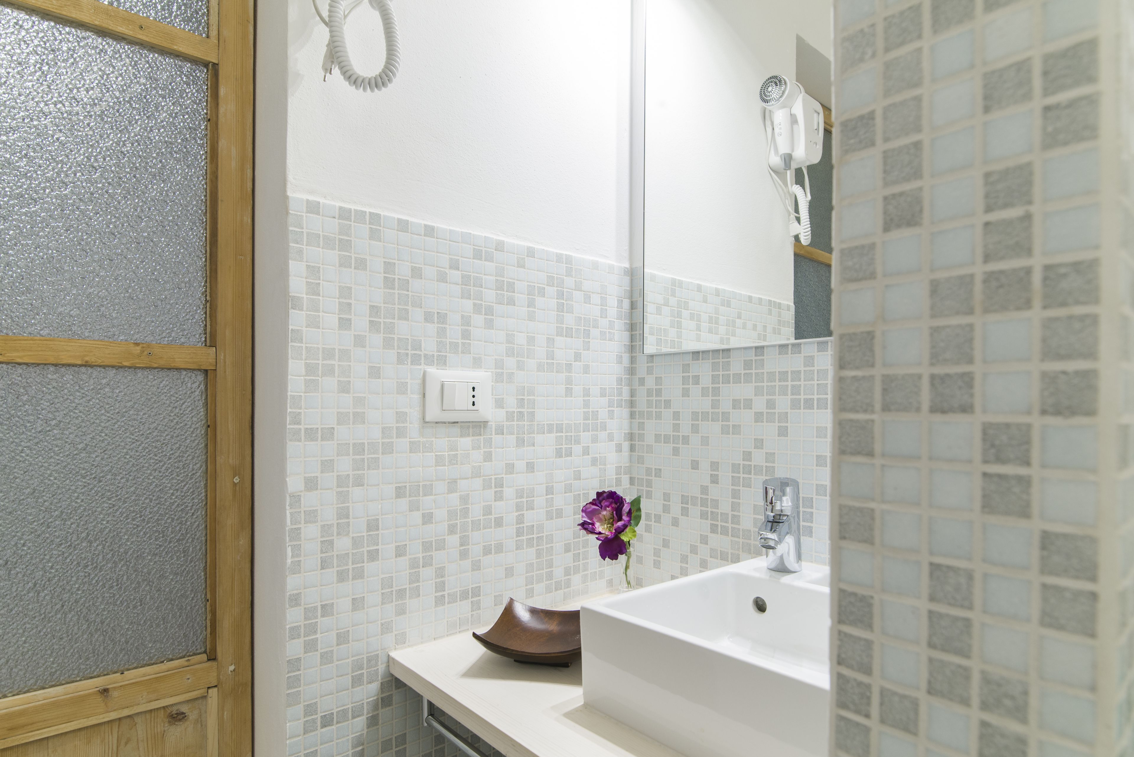 Un baño con lavamanos blanco, espejo y zona de ducha.