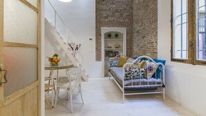 A cozy room with a white bed, a dining table with chairs, a staircase, and a brick wall. - University Loft Apartment (Bologna)
