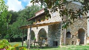 A stone building with a balcony, arched windows, and a wooden table with chairs in the foreground. - Villa Acquavella (Casal Velino)