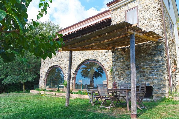 Un edificio de piedra con una pérgola, mobiliario exterior y ventanas en arco.